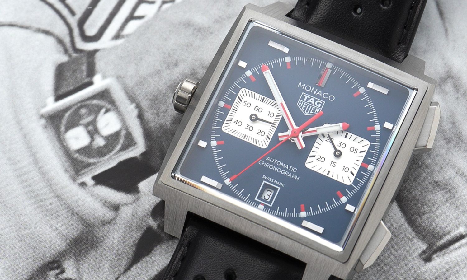 TAG Heuer Monaco 2026 Blau CDW2181.FC8360 mit blauem Zifferblatt am schwarzen Lederarmband liegend von vorne abgebildet mit einem schwarz-weißen Bild eines klassischen TAG HEUER Monaco Modells