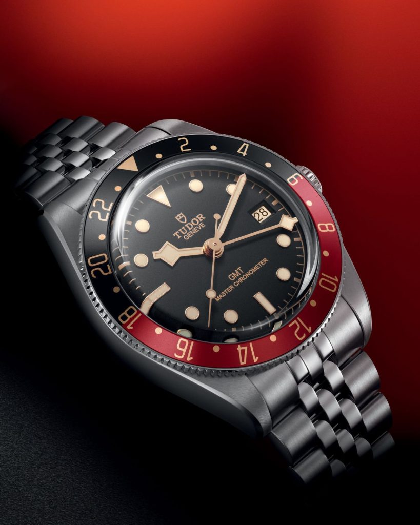 TUDOR Black Bay 58 GMT mit schwarzem Zifferblatt und schwarz-roter Lünette aus halblinker Ansicht vor schwarz-rotem Hintergrund.