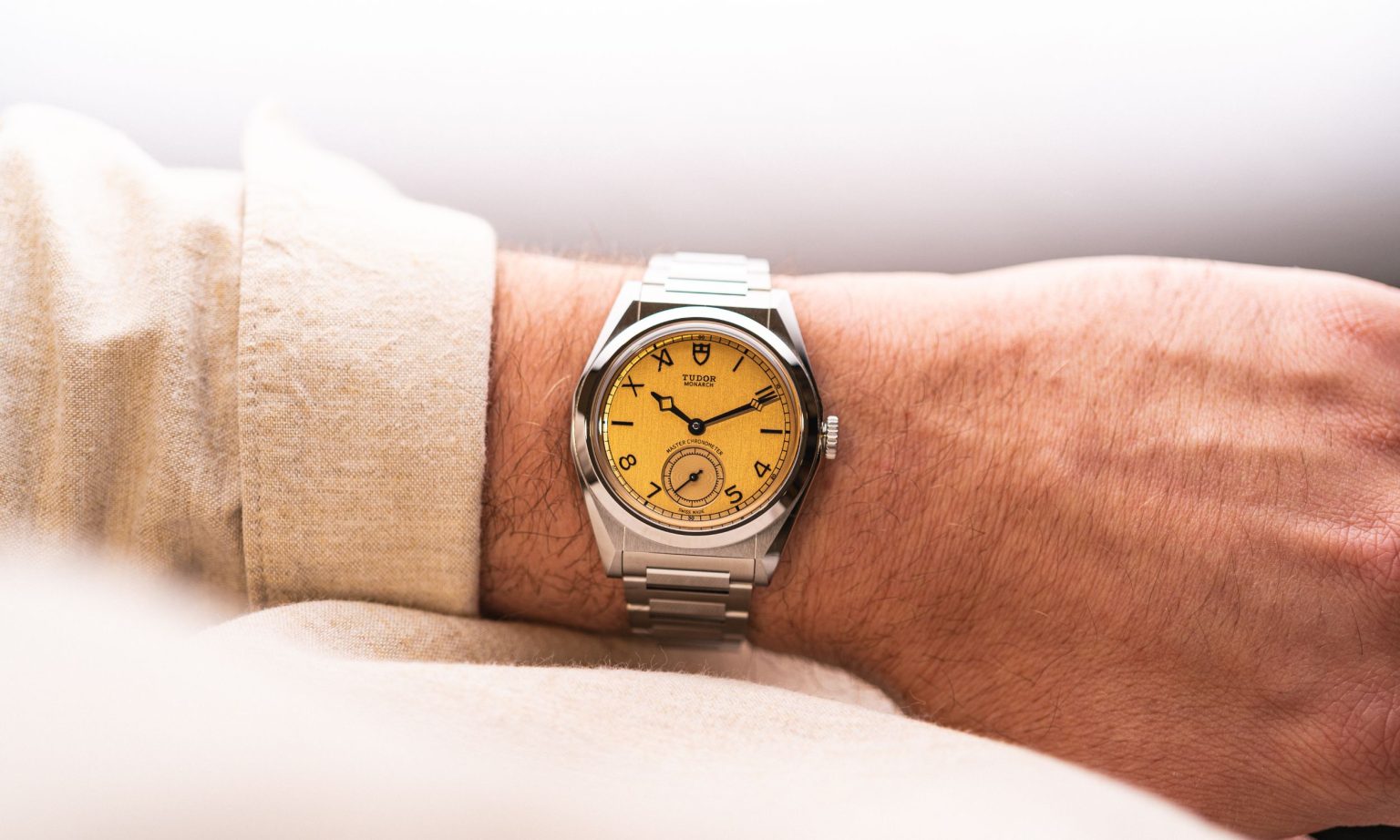 Wristshot der TUDOR Monarch vor hellem Hintergrund mit beigem Hemd.